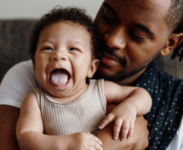 A joyful infant laughing while being held by the father