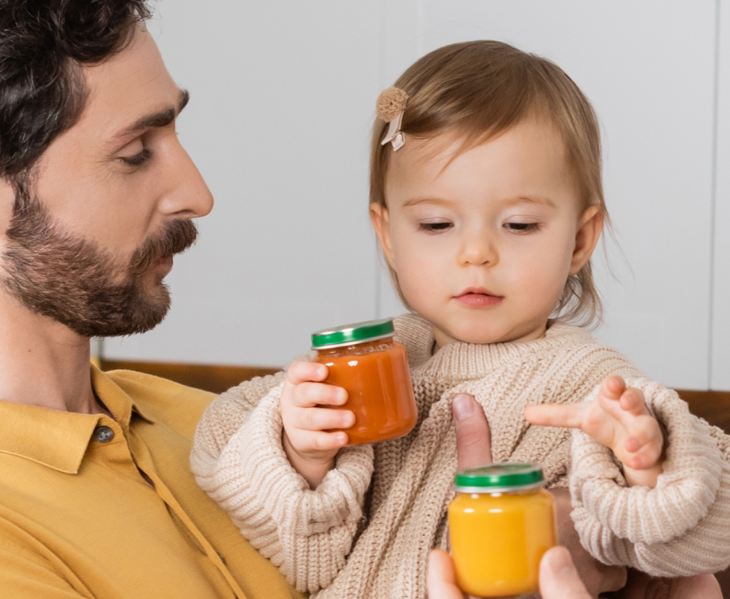 A father in a kitchen holding his toddler while also holding a cup.